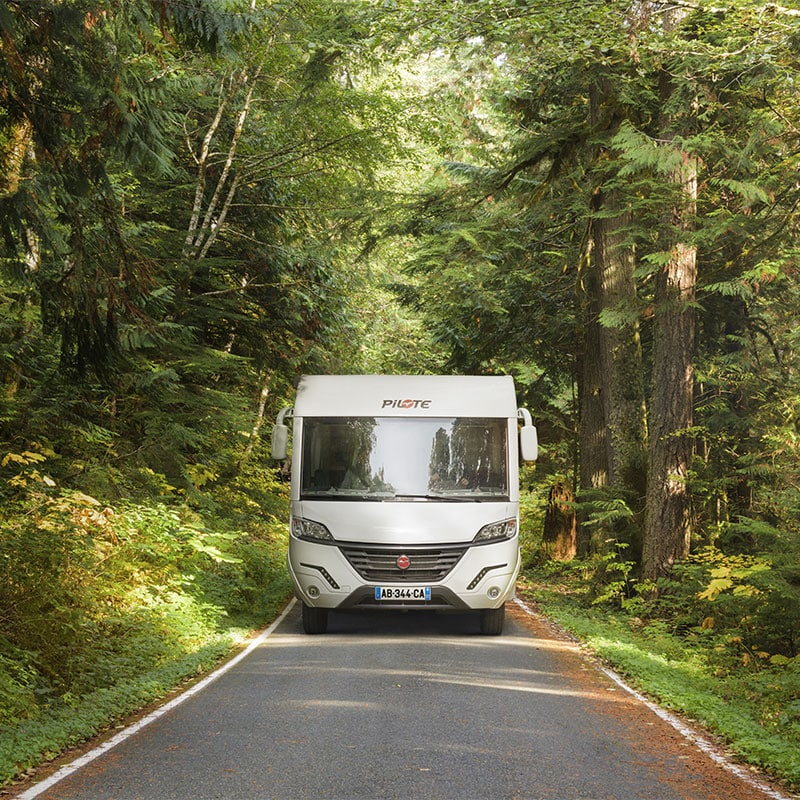 Camping-car profilé Pilote sur une petite route au milieu des champs verdoyants.
