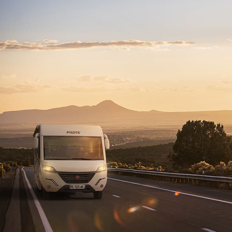 Camping-car intégral Pilote sur une large route au soleil couchant.