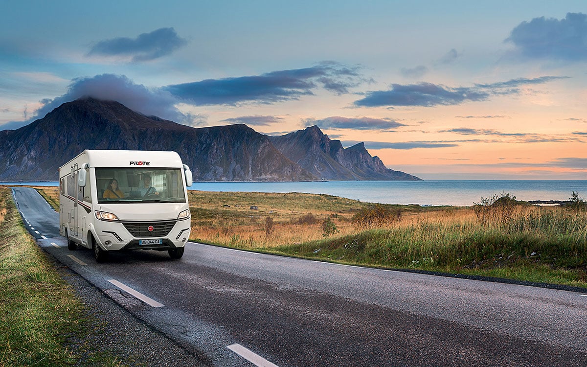 Camping-car intégral Pilote roulant sur une route le long d'un lac, le soleil se couchant au loin.
