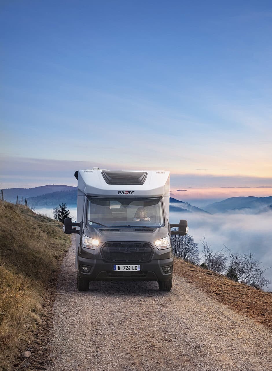 Camping-car profilé étroit Pilote sur un chemin caillouteux, au dessus d'une mer de nuages.